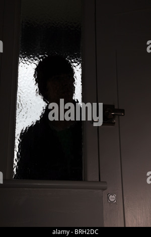Silhouette male intruder looking through an opaque window next to a front door Stock Photo