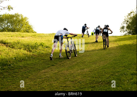 Athletes taking part in the Basildon off-road triathlon struggle with their bikes on hill. Gloucester Park in Basildon, Essex. Stock Photo