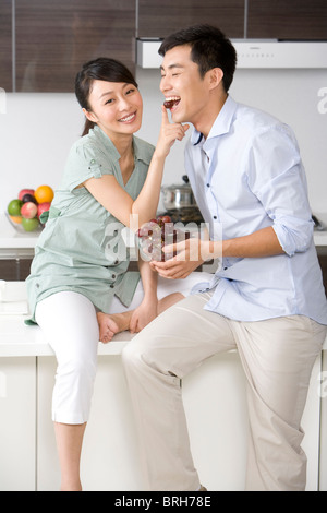 Woman feeding man grapes in the kitchen Stock Photo