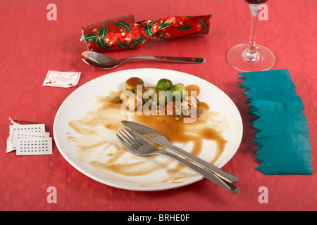 finished christmas dinner with sprouts left on white dinner plate on red tablecloth christmas cracker opened Stock Photo