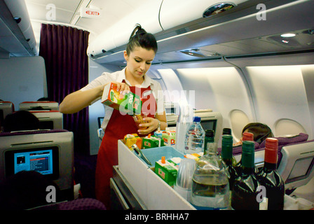Long haul flight air stewardess with food drinks aisle trolley on overnight Virgin Atlantic aircraft serving drink to passenger Stock Photo