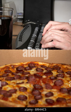 software engineer pulling an all nighter typing at a keyboard with cola and pizza Stock Photo