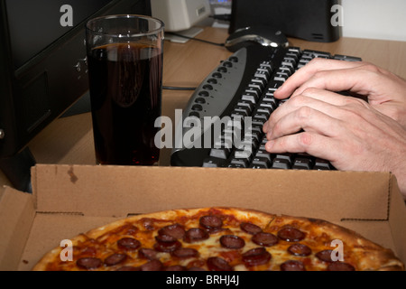 software engineer pulling an all nighter typing at a keyboard with cola and pizza Stock Photo