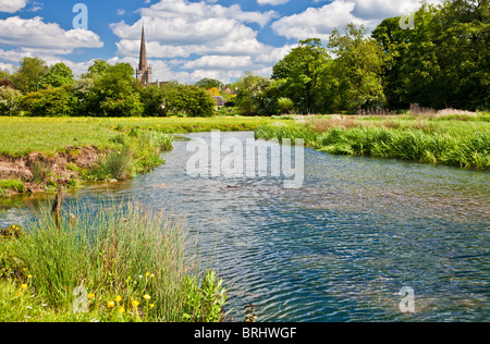 Summer view across meadow and River Windrush to St John the Baptist Church in Cotswold town of Burford, Oxfordshire, England, UK