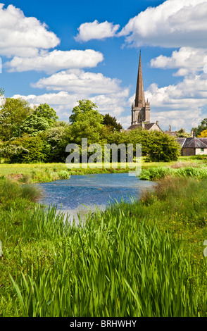 Summer view across meadow and River Windrush to St John the Baptist Church in Cotswold town of Burford, Oxfordshire, England, UK