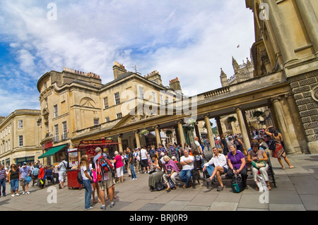 Horizontal wide angle of crowds of tourists and people walking by and sitting by the historic Roman Baths in Bath city centre Stock Photo