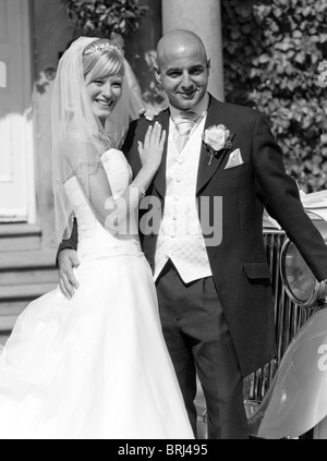 A bride and groom pose for guests in front of their vintage wedding car Stock Photo