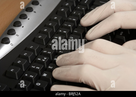 hands wearing surgical rubber white gloves typing at a computer keyboard Stock Photo