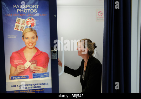 Photo booth woman preparing to have passport picture taken using public portrait machine Stock Photo