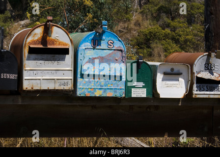 A row of colorful, weathered US mailboxes lined up on Sunset Way, Muir beach, CA, featuring rustic metal, peeling paint, and hand-painted designs. Stock Photo