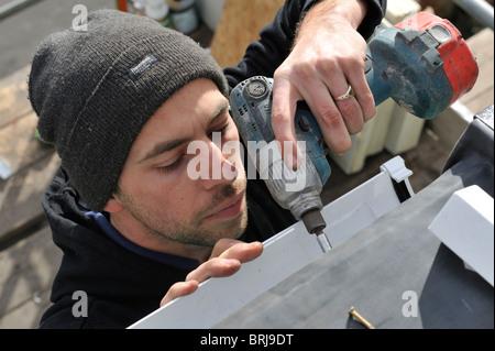 Man using cordless screwdriver fitting gutter Stock Photo
