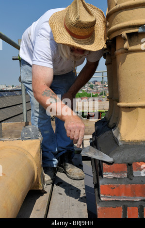 Builder re-pointing flaunchings on brick chimney stack Stock Photo