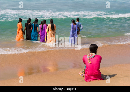 A group of traditionally dressed Indian women paddling in the sea on Kovalam beach, Kerala, India. Stock Photo