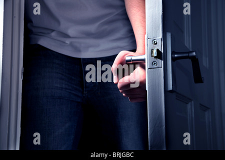Caucasian hand turning the handle opening a door and entering a dark room Stock Photo