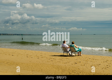 Elderly couple sat on deck chairs at seaside Stock Photo