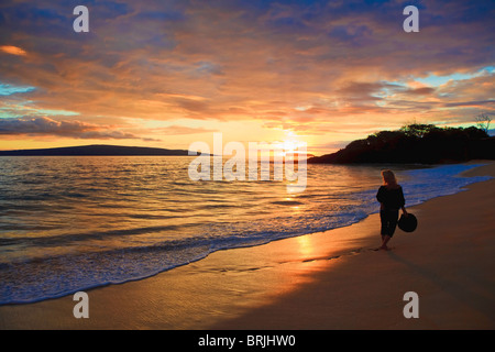 beautiful middle age woman walking on the shore alone on makena beach, maui at sunset Stock Photo