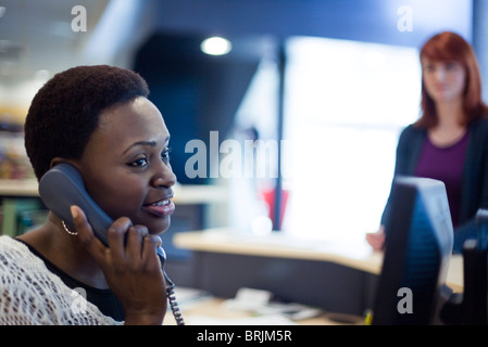 African american receptionist talking at landline phone being ...