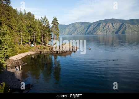 A young adult couple skip rocks as there friends kayak next to the camping site in Idaho. Stock Photo