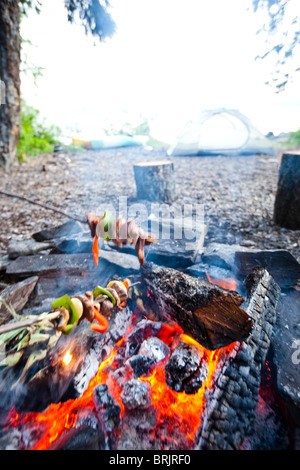 Young adults cook shish kabobs over the fire on a camping trip in Idaho. Stock Photo