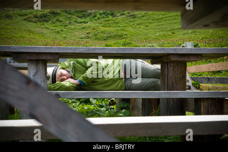 A young woman takes a nap on a bench after a long hike and filling lunch in the Swiss Alps. Stock Photo