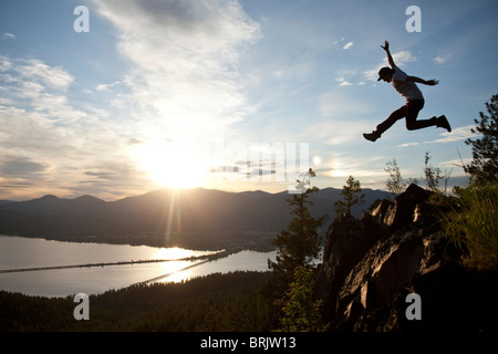 Young man soaring at sunset next to a large cliff overlooking  a lake. Stock Photo