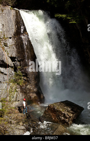 A young man stands at the base of a waterfall looking up. Stock Photo