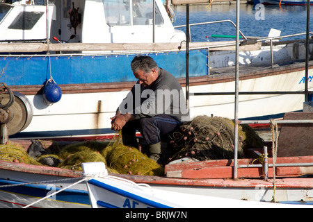 Fisherman mending nets on a boat moored to the quay side in Skala Kallonis; Lesvos Stock Photo