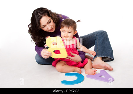 Mother, nanny, or teacher teaching happy baby to learn alphabet, A, B, C, with letters in a playful way, while sitting on floor. Stock Photo