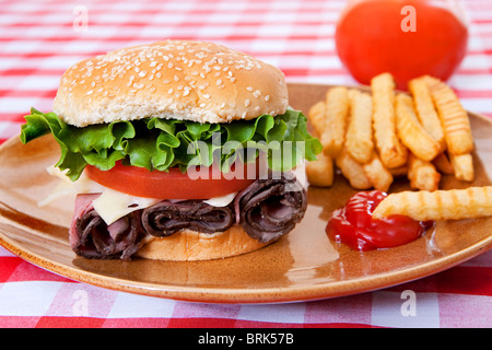 one large roast beef sandwich in sesame roll with tomatos and lettuce on plate with classic red and white checkered tablecloth Stock Photo