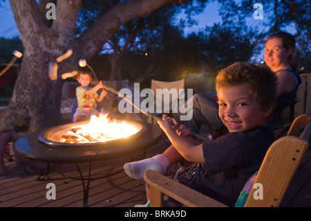 A family toasting marshmallows over a fire in their backyard. Stock Photo