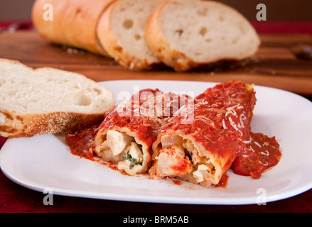 two tasty stuffed manicotti shells topped with pasta sauce and Italian bread on the side Stock Photo