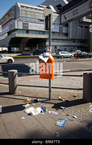 Overflowing trash bin with litter scattered on the ground in an urban area of Berlin. Stock Photo