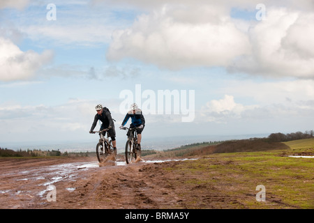Couple riding mountain bikes through mud Stock Photo