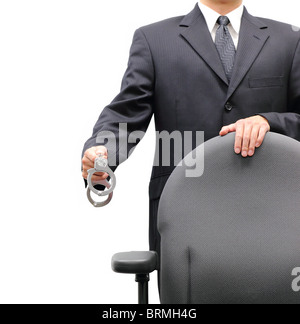 Business man standing behind an office chair holding a pair of handcuffs, isolated on a white background. Stock Photo