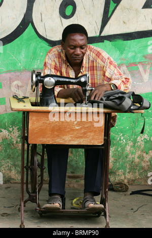 A tailor sitting outside a shop working on a  sewing machine Stock Photo