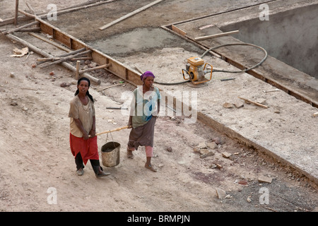 Two female construction workers carrying wet cement in a bucket carried on a pole between them Stock Photo