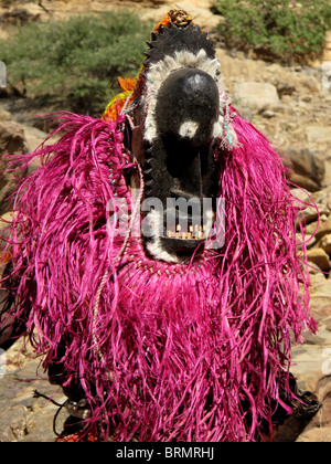 Portrait of a Dogon dancer wearing a carved wooden mask and brightly coloured pink headdress performing a ceremonial dance Stock Photo