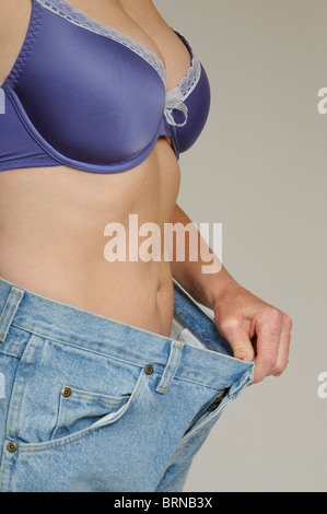 Weight loss Woman holding out waistband of her jeans after loosing several inches on her waist measurement Stock Photo