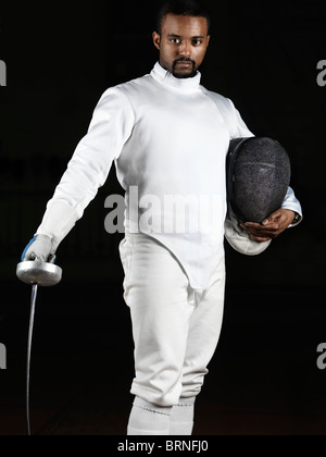 Portrait of a fencer wearing fencing uniform and holding an epee and a mask isolated on black background Stock Photo