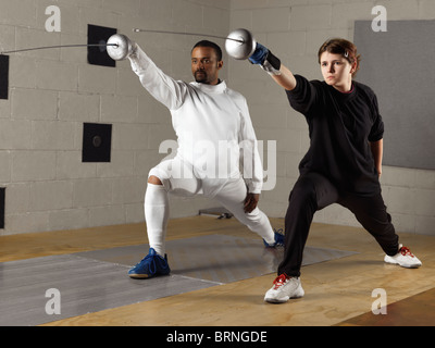 Coach and a teenage student practicing fencing in a gym Stock Photo