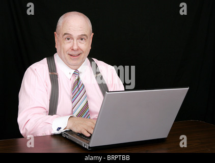 happy business man in a pink shirt on a black background working on a laptop computer Stock Photo