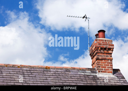 TV aerial on a house slate roof with red brick chimney stack UK Stock Photo