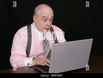 business man in a pink shirt surprised on a black background working on a laptop computer Stock Photo