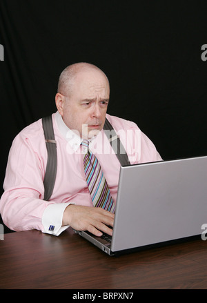 business man in a pink shirt on a black background working on a laptop computer Stock Photo