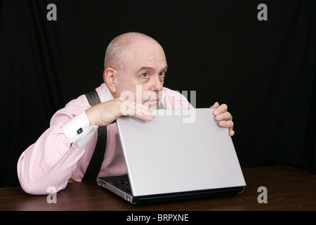 business man in a pink shirt on a black background protecting his laptop computer Stock Photo