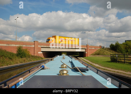A narrow boat passing under a busy road on the Trent and Mersey Canal. Stock Photo