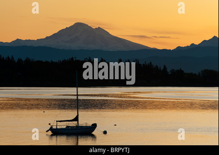 A sailboat at anchor off Lummi Island, Washington with Mt. Baker in the background during a magnificent sunrise. Stock Photo