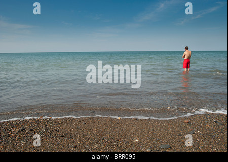 A man on holiday standing alone in the sea wearing red shorts, Aberystwyth wales UK Stock Photo