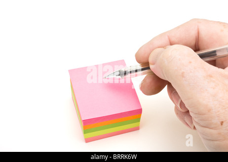 Block of vibrant multicoloured Post it Notes isolated on white with hand holding pen and copy space. Stock Photo