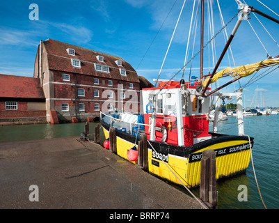 Yellow commercial shell fishing trawler moored alongside quay at Ashlett on Southampton Water with old mill red brick building Stock Photo